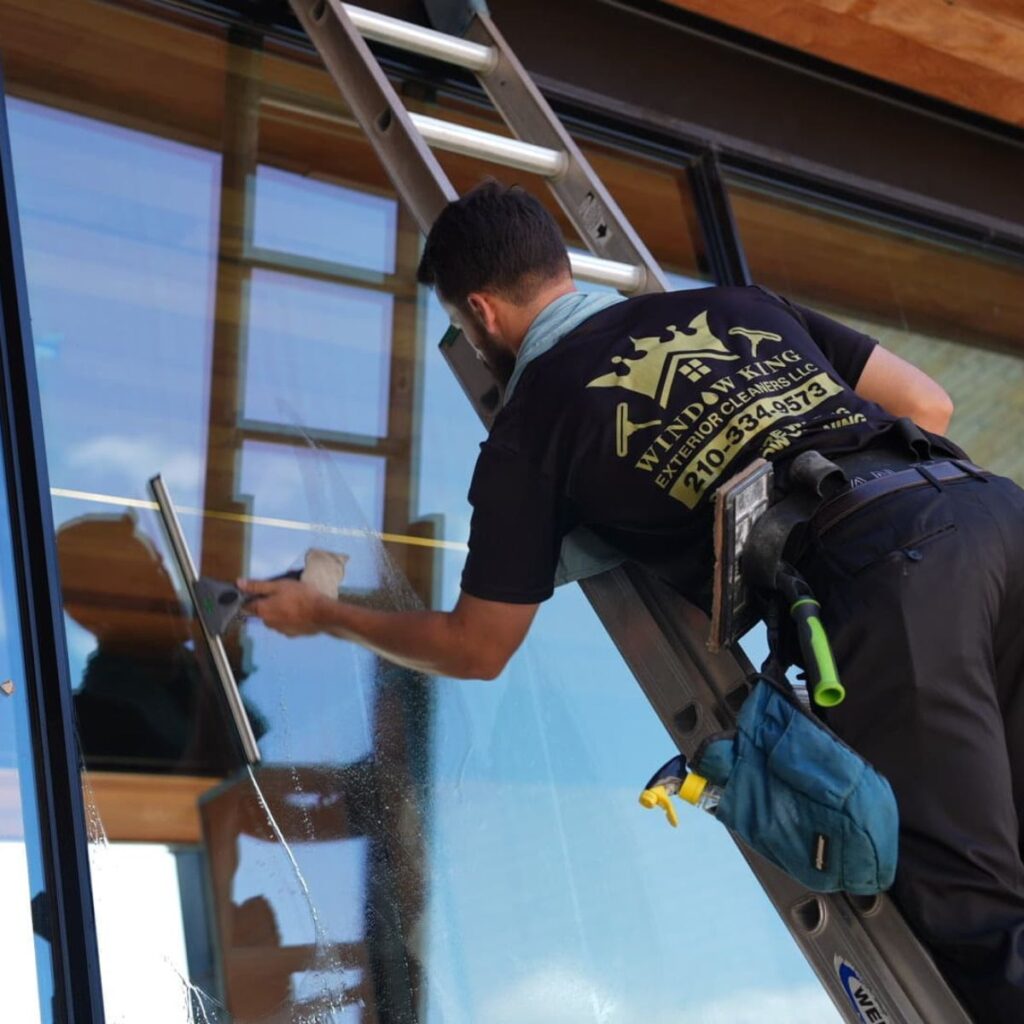 Technician on ladder uses a squeegee to clean large residential windows