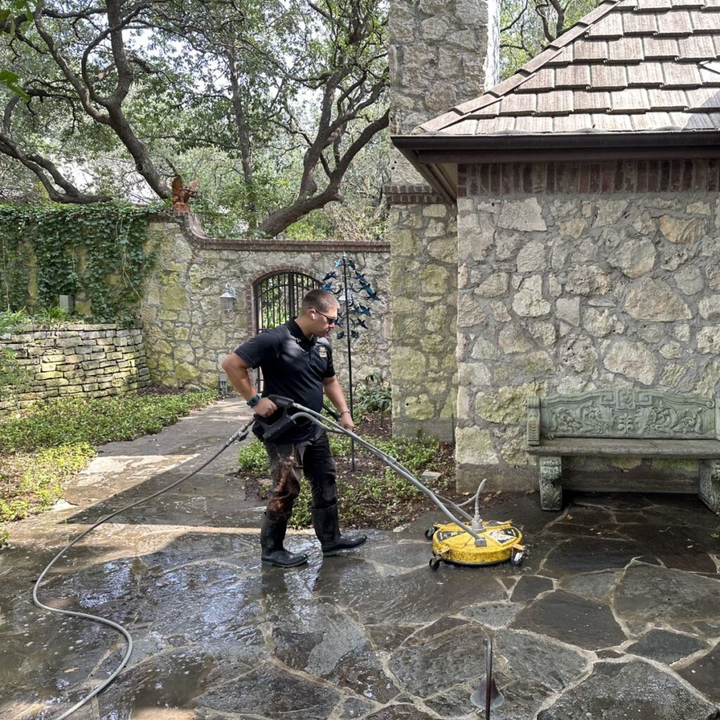 Technician power washes a stone patio in a landscaped residential backyard