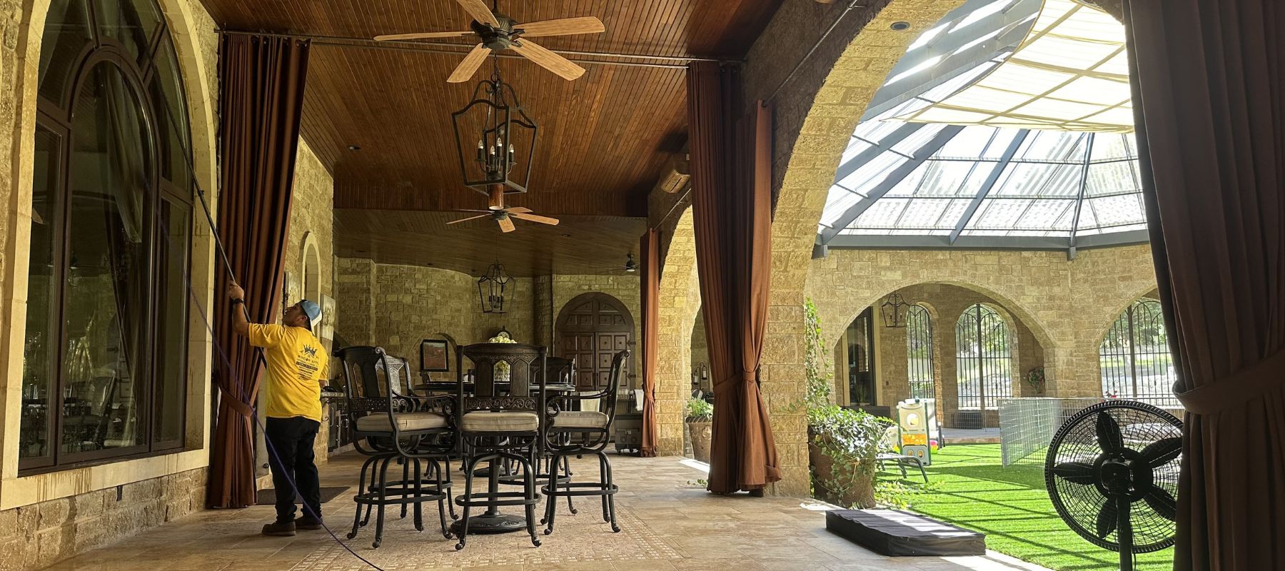 Technician using a long extension pole to clean large arched windows on a luxurious covered patio
