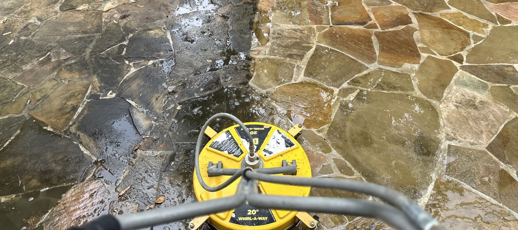 Close-up of a yellow surface cleaner power washing flagstone with a clear before-and-after result
